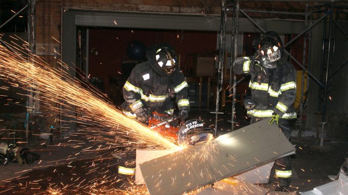 Firefighters cut apart a garage door so that other firefighters can gain access to the fire in a room and stairway behind the garage at 50 La Loma Drive in Menlo Park. Photo by Peter Mootz, courtesy of the Menlo Park Fire Protection District.